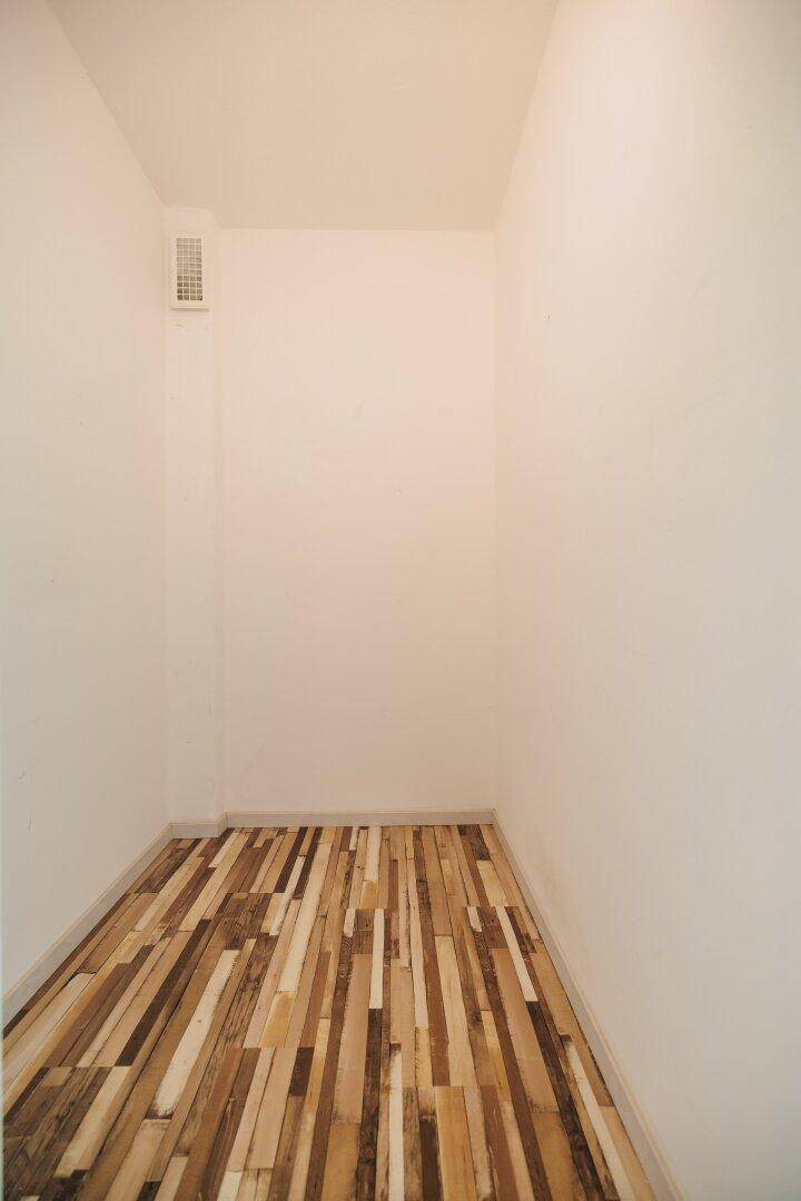 Kleiner Abstellraum mit einzigartigem Holzbodenmuster und weiß gestrichenen Wänden.