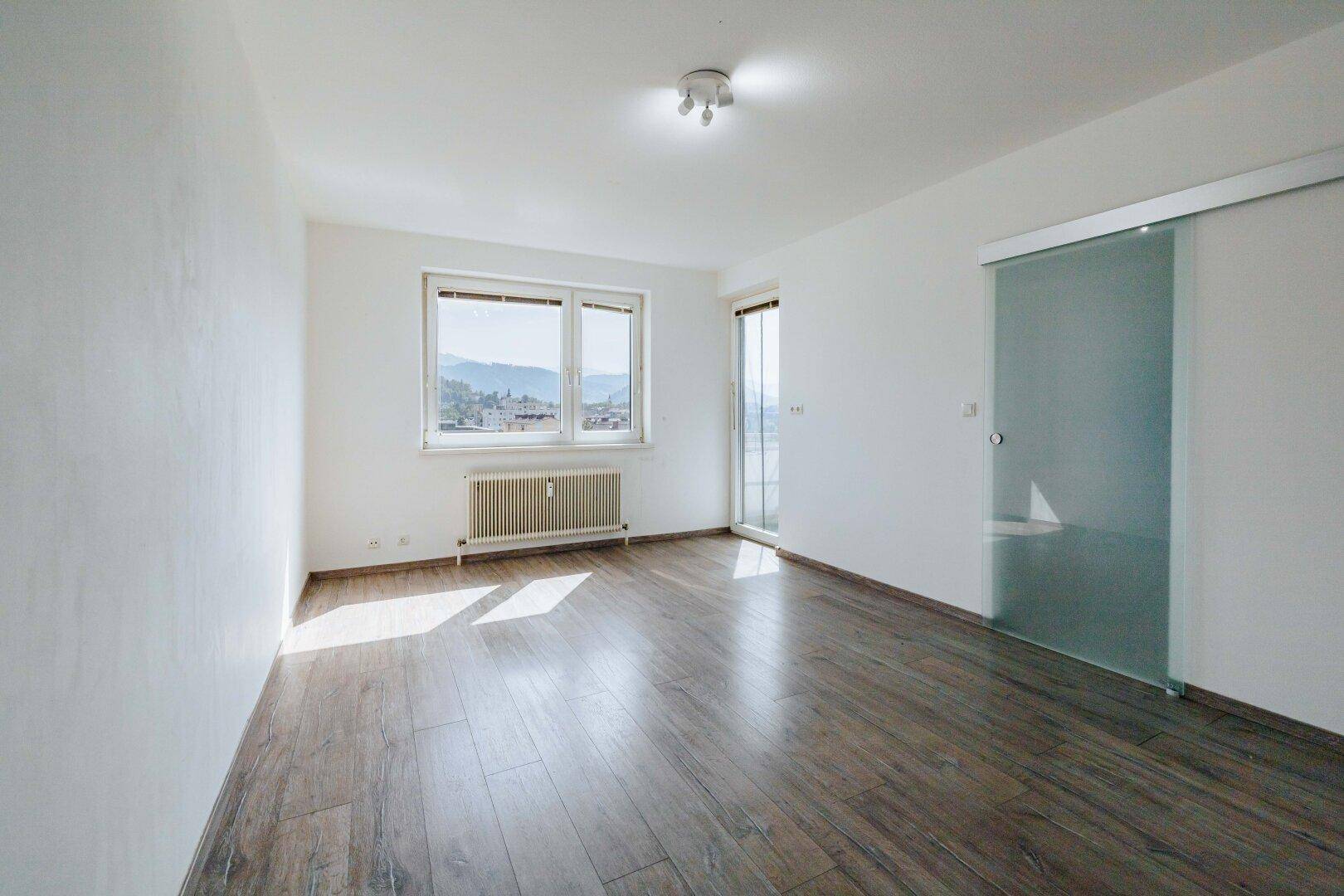 Heller Wohnraum mit Laminatboden, großen Fenstern und viel natürlichem Licht.