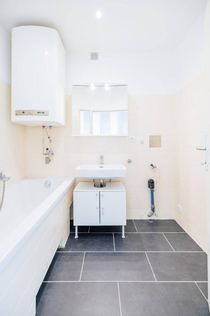 Badezimmer mit Badewanne, Waschbecken, Spiegelschrank und Wandboiler.