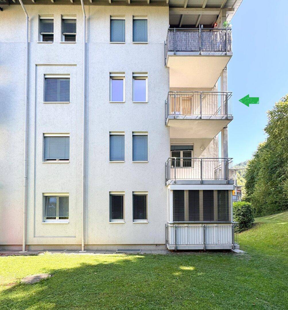 Fassade eines Mehrfamilienhauses mit Balkonen und grüner Umgebung.