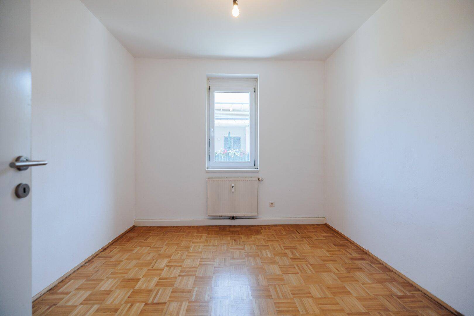 Kleineres Schlafzimmer mit Parkettboden, weißen Wänden und einem Fenster.