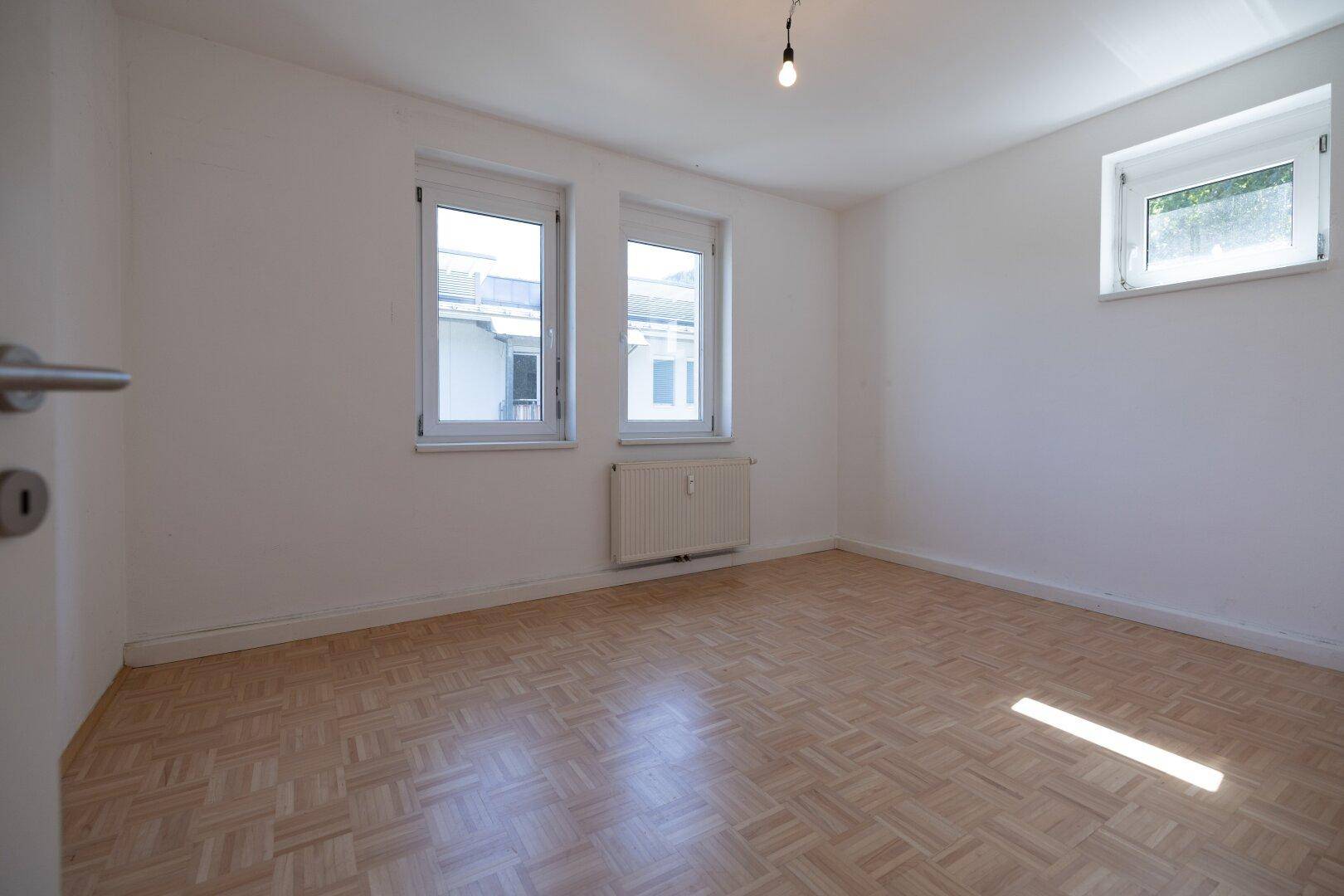 Geräumiges Schlafzimmer mit Parkettboden, weißen Wänden und mehreren Fenstern.