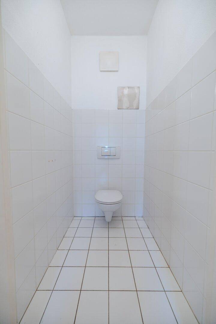 Separates WC mit weißen Fliesen und wandhängender Toilette, funktional und hell.