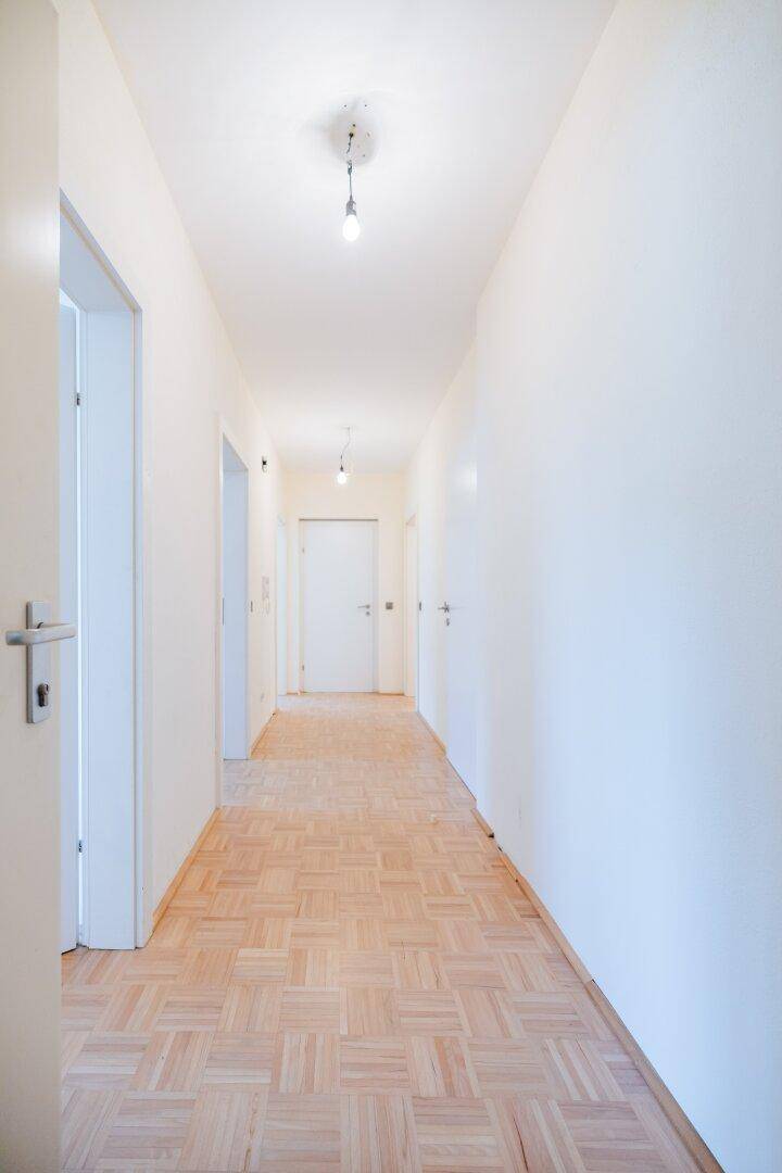 Langer, heller Flur mit Parkettboden und mehreren weißen Türen zu den Zimmern.