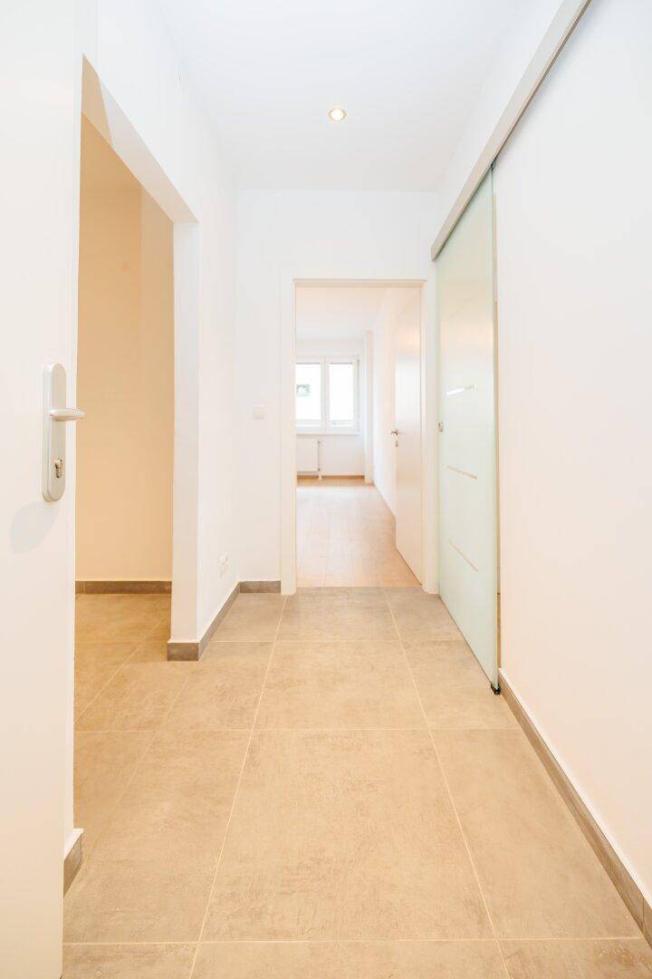 Heller Flur mit beigefarbenen Fliesen und einer modernen Glasschiebetür.