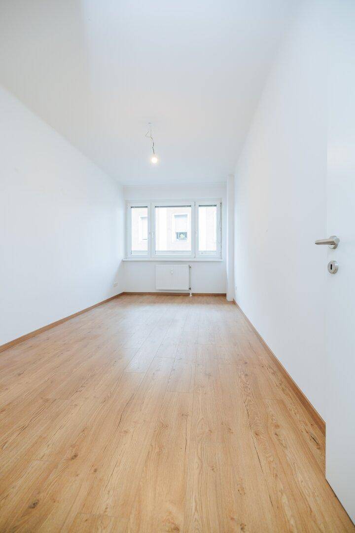 Langes, helles Zimmer mit Holzboden und Fenster, ideal als Schlaf- oder Arbeitszimmer.