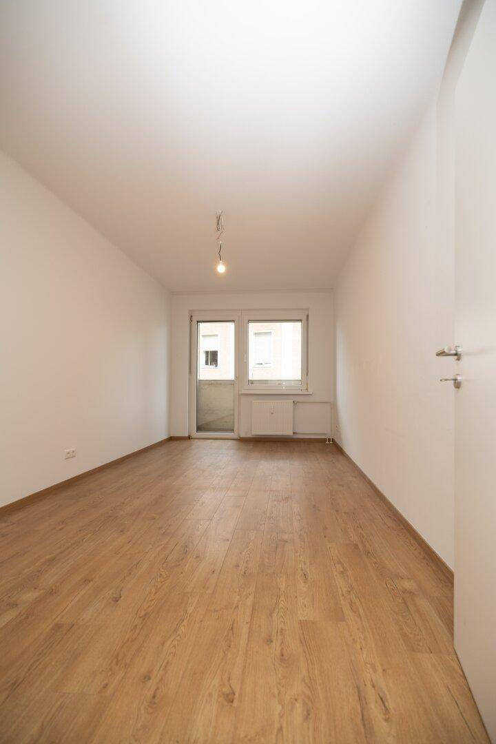 Helles Zimmer mit Holzboden und Zugang zu einem Außenbereich, bereit zur individuellen Gestaltung.