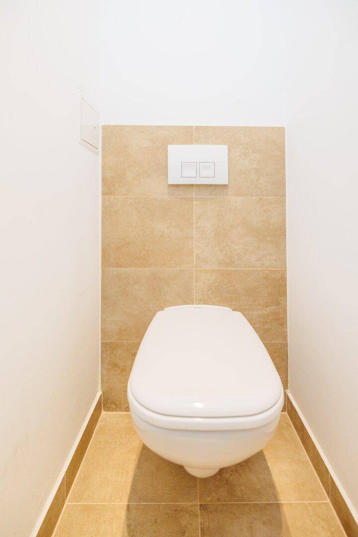 Separates WC mit wandhängender Toilette und beigefarbenen Fliesen an Wand und Boden.