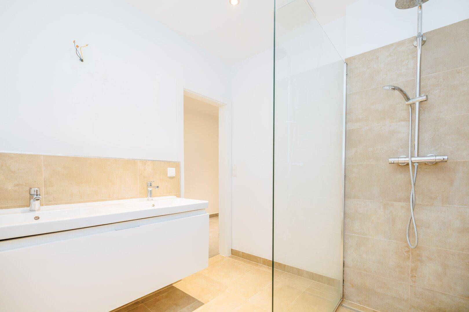Modernes Badezimmer mit begehbarer Dusche, Einzelwaschbecken und beigefarbenen Fliesen.