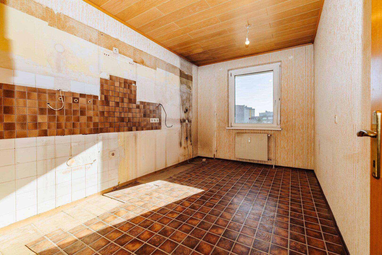 Renovierungsbedürftige Küche mit braunen Fliesen, Fenster und Holzdecke.