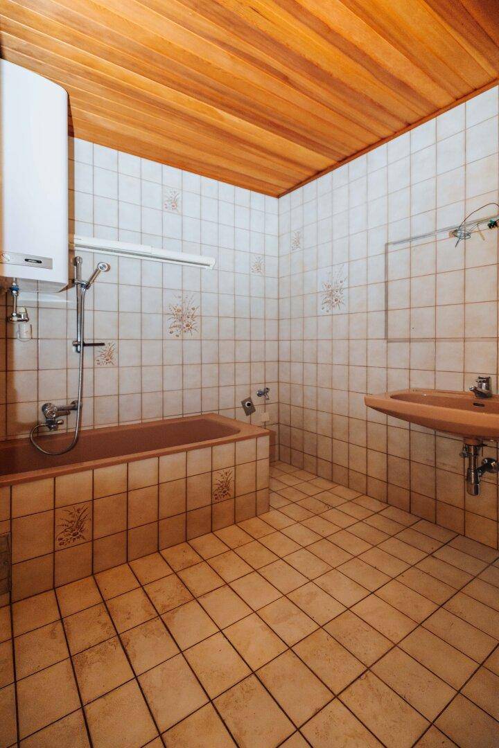 Badezimmer mit Badewanne, Waschbecken, Fliesen und Holzdecke.
