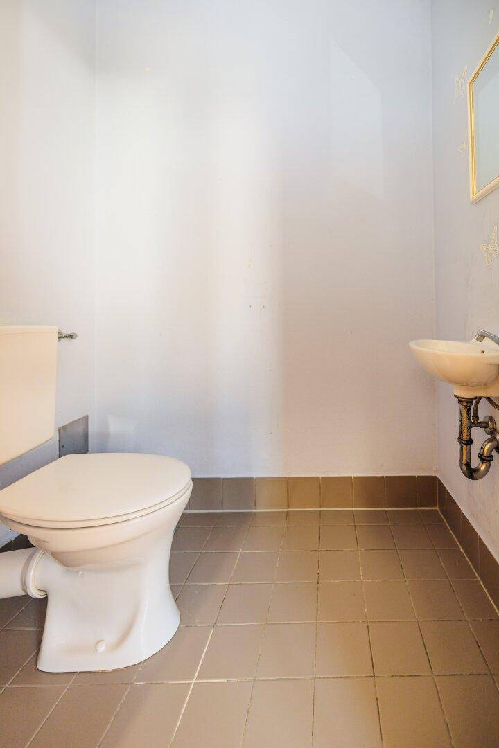 Kleines Gäste-WC mit Toilette, Waschbecken und Fliesenboden in neutralen Farbtönen.