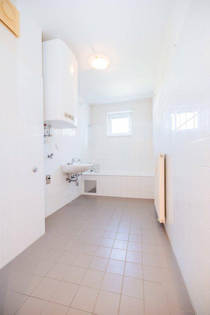 Helles Badezimmer mit weißen Fliesen, Waschbecken, Badewanne und Fenster für natürliche Belüftung.