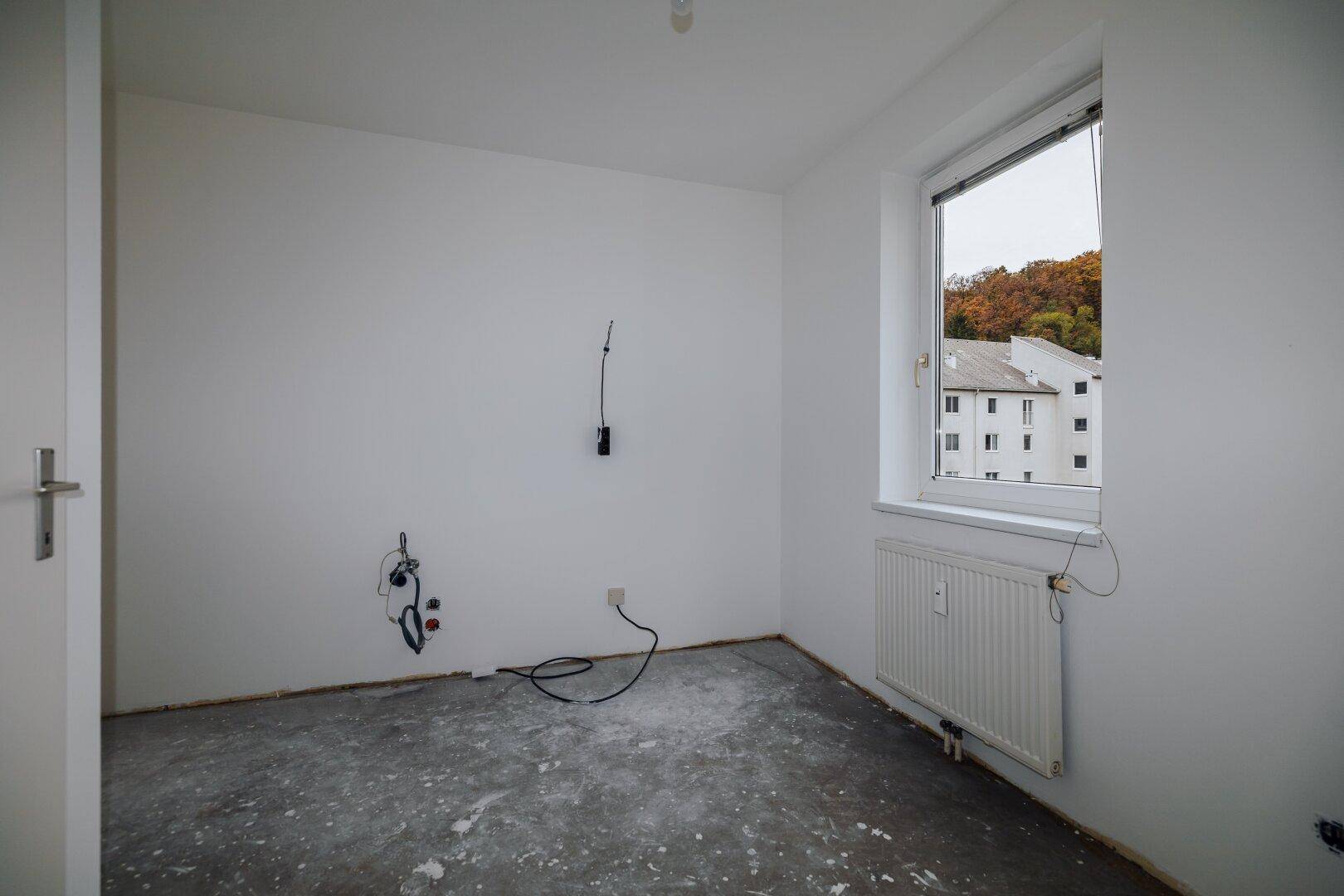 Leeres Schlafzimmer mit weiß gestrichenen Wänden, Fenster und Heizkörper, bereit zur Gestaltung.