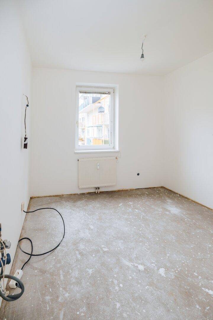 Heller Raum mit Fenster und Heizkörper, ideal als Schlafzimmer oder Arbeitszimmer, mit Blick nach draußen.