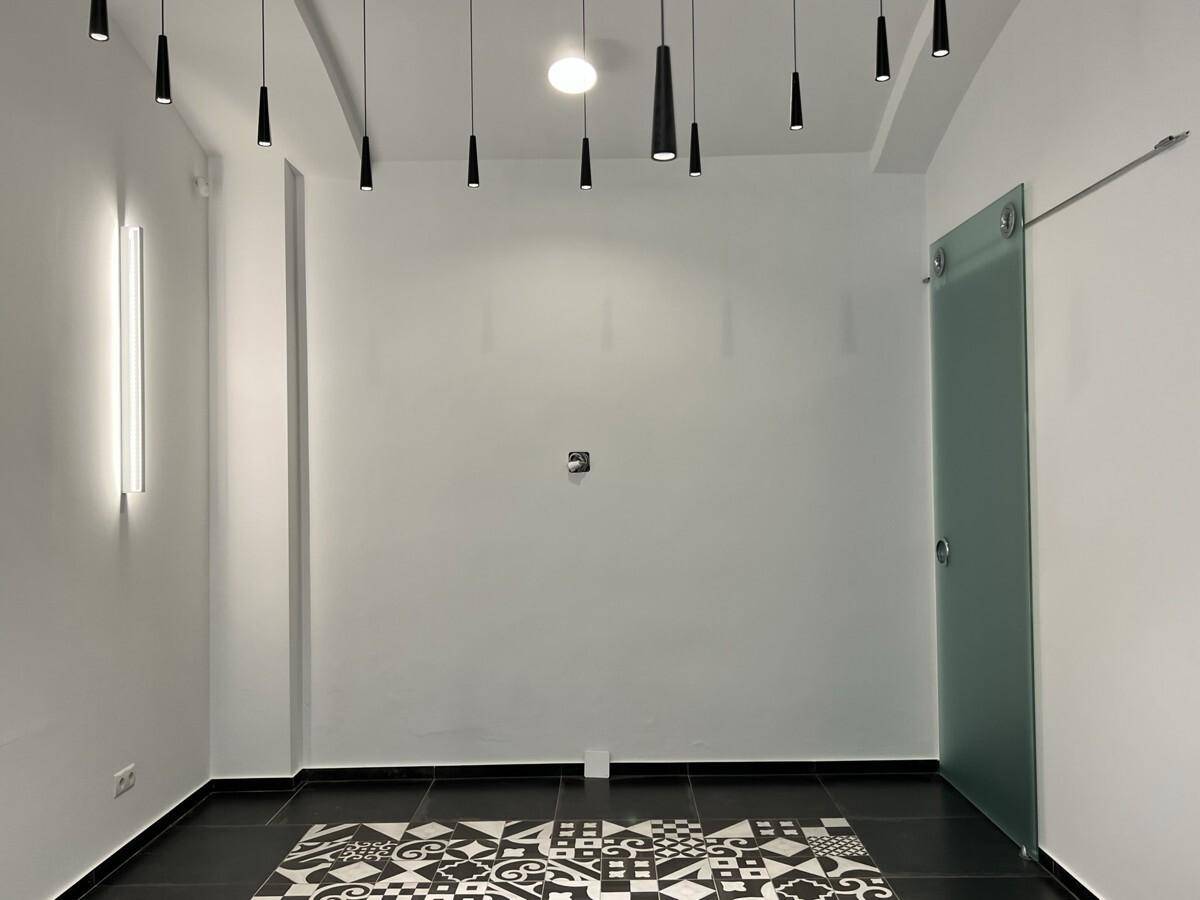 Moderner Raum mit einer Glasschiebetür, Deckenstrahlern und einem gemusterten Fliesenboden.