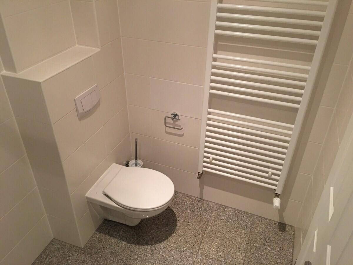 Modernes WC mit wandhängender Toilette, beigefarbenen Fliesen und Handtuchheizkörper.