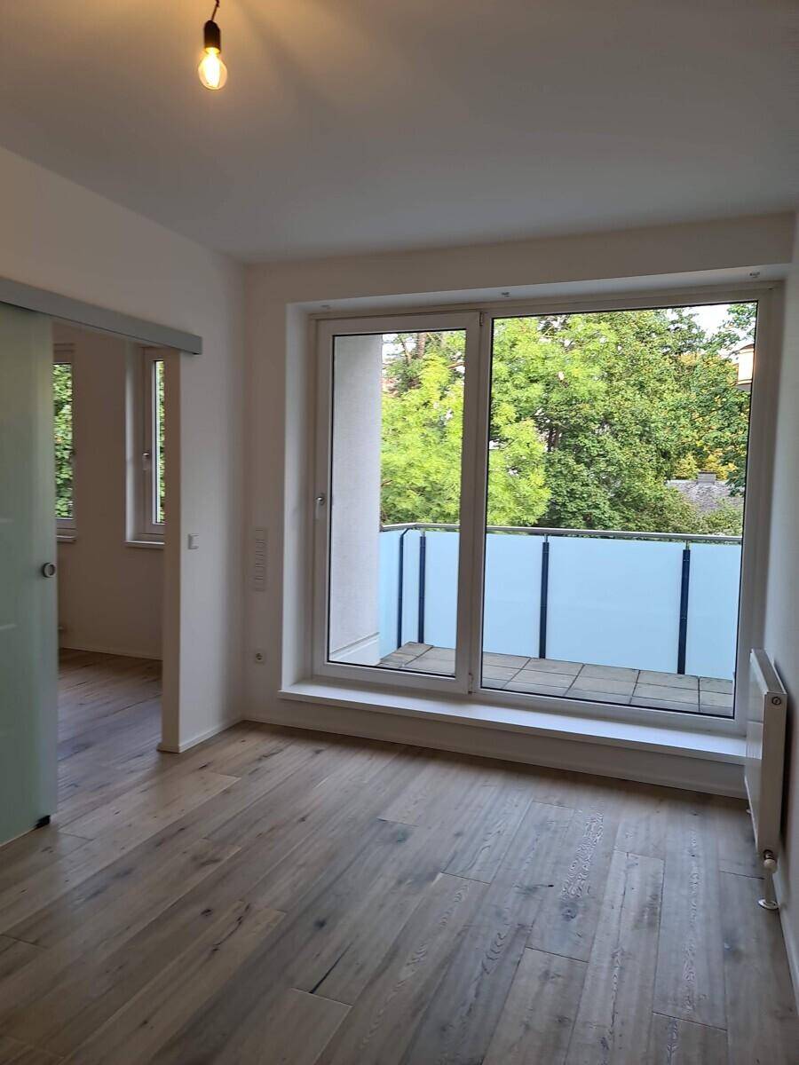 Geräumiges Zimmer mit Holzboden und großem Fenster mit Zugang zum Balkon.