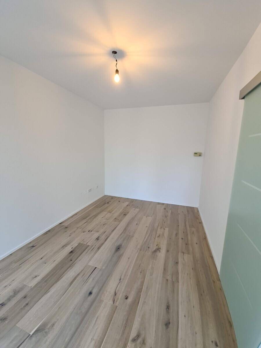 Leeres Zimmer mit Holzboden und einer modernen Schiebetür, bereit zur individuellen Gestaltung.