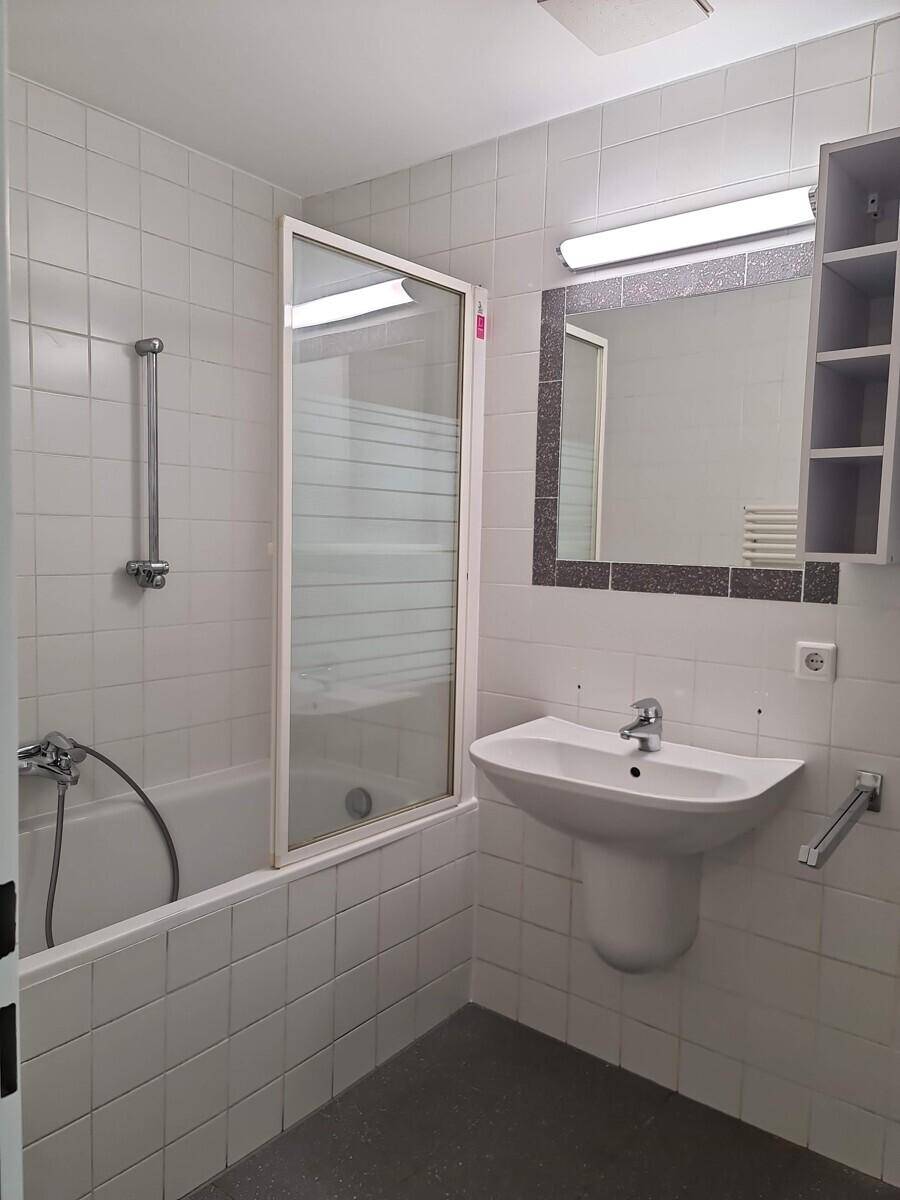 Helles Badezimmer mit Badewanne, Glasduschwand, Waschbecken und Spiegelschrank.