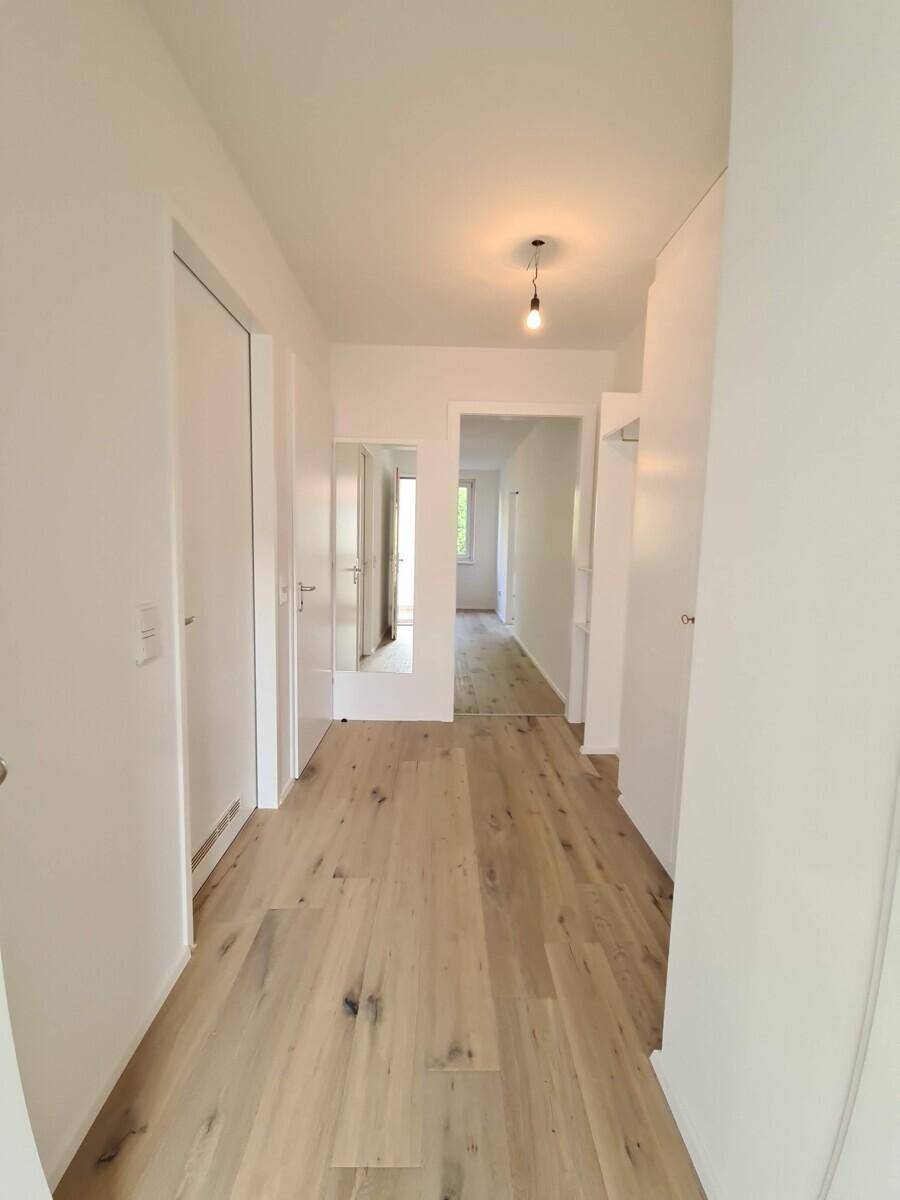Heller Flur mit Holzboden und weiß gestrichenen Wänden, der zu weiteren Räumen führt.