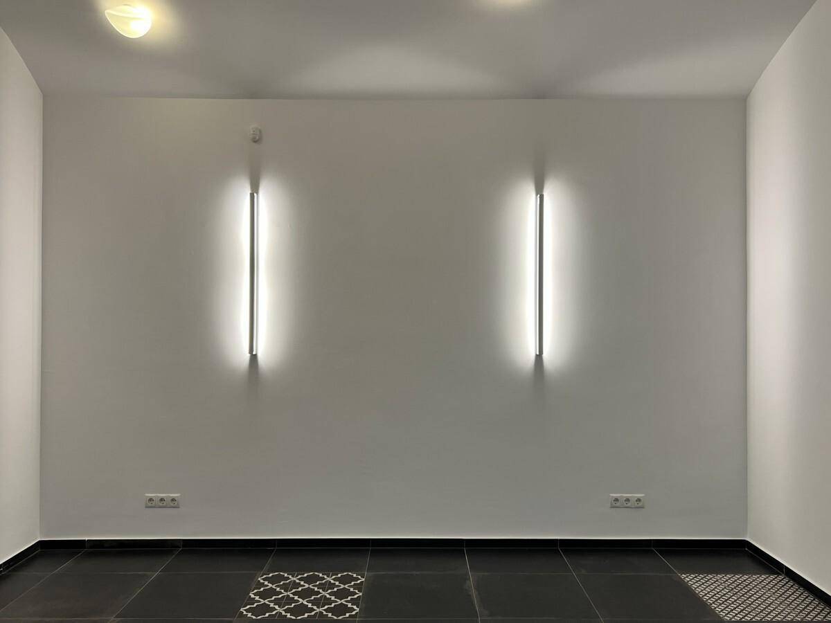 Leerer Raum mit modernen vertikalen Wandleuchten und einem gemusterten Fliesenboden, bereit zur Einrichtung.