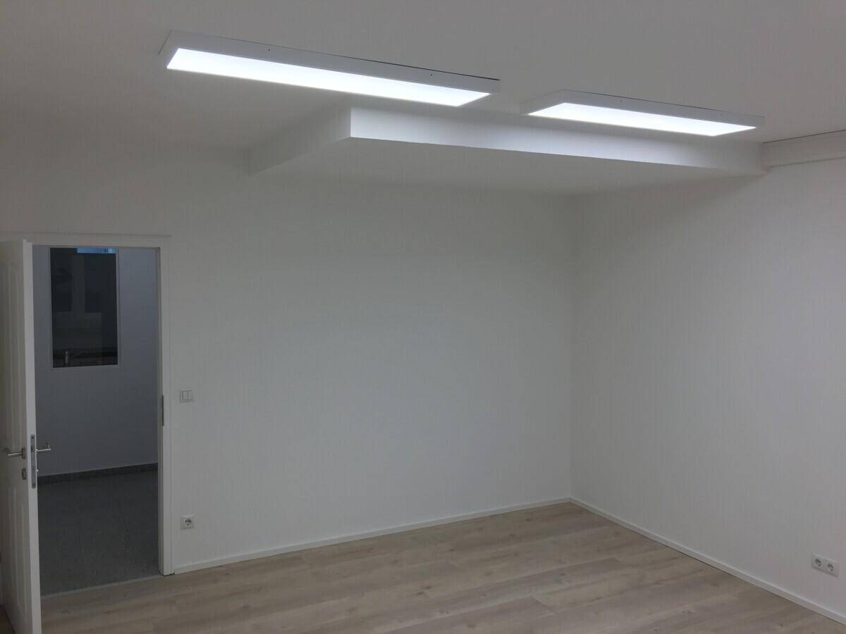 Sauberer Büroraum mit weißem Anstrich, hellem Laminatboden und Deckenbeleuchtung.