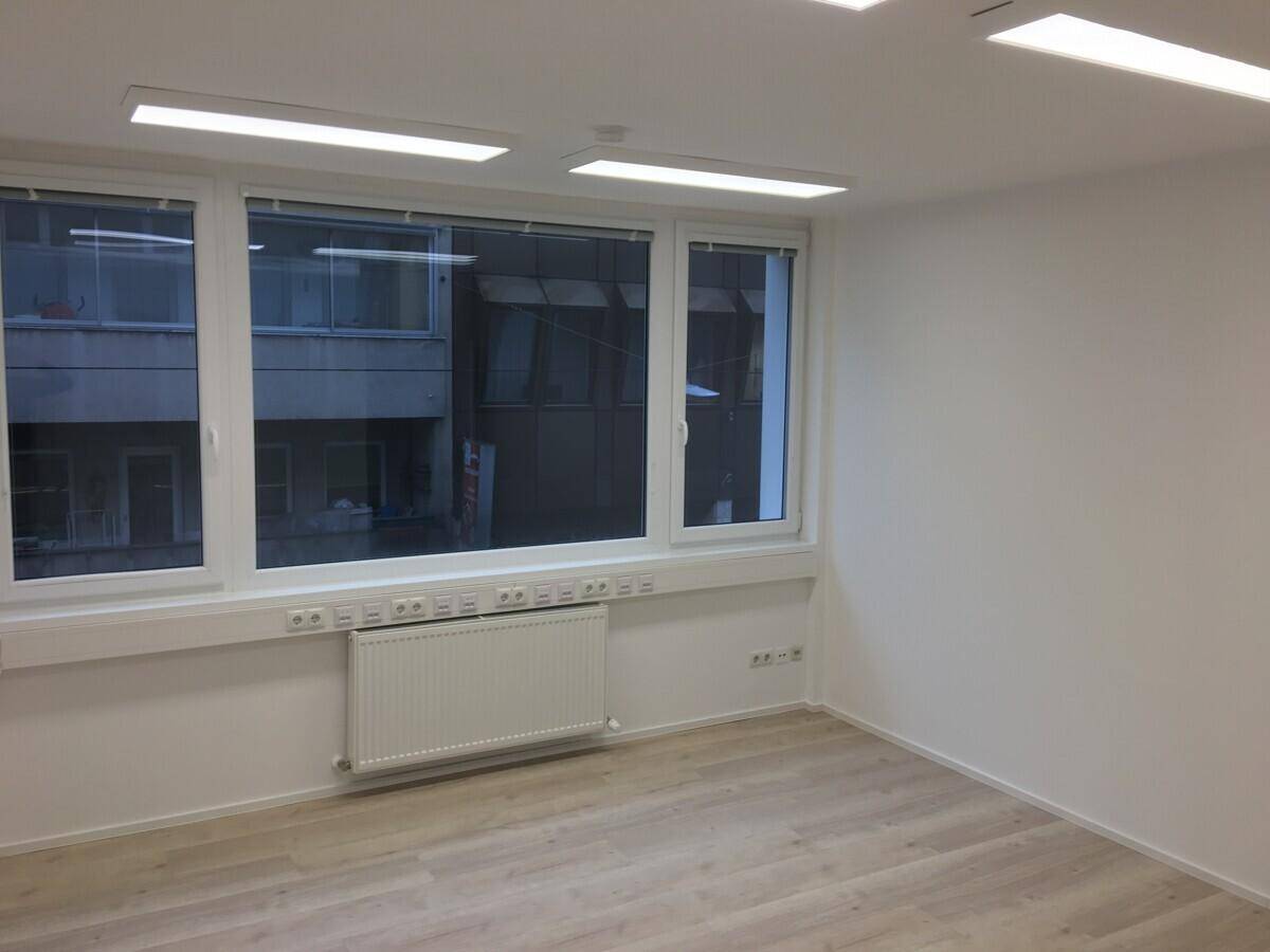 Leerer Büroraum mit hellen Wänden, modernem Laminatboden und Blick auf umliegende Gebäude.