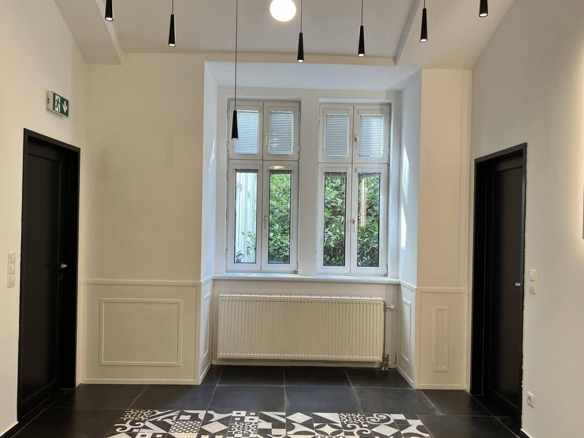 Heller Flur mit einem großen Fenster, das einen Blick ins Grüne bietet, und dunklen Türen.