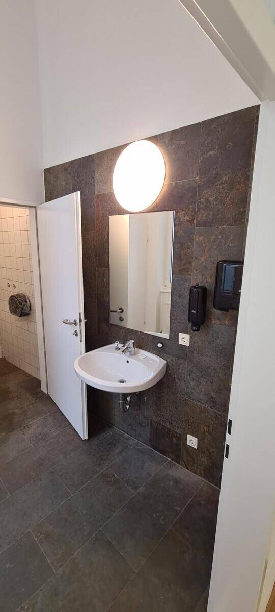 Modernes Badezimmer mit Waschbecken, Spiegel und dunklen Fliesen an Wand und Boden.