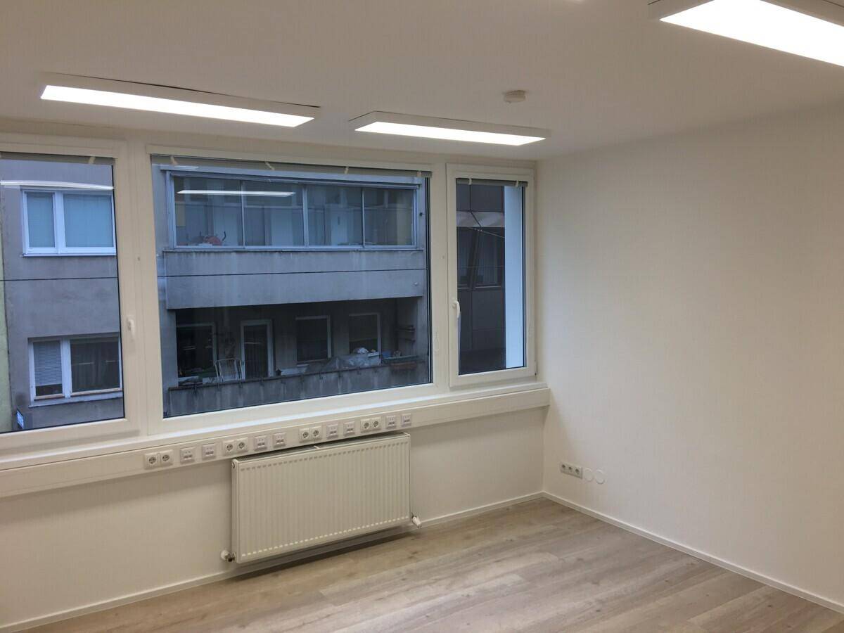 Heller Büroraum mit Laminatboden, großen Fenstern und Blick auf die umliegende Bebauung.