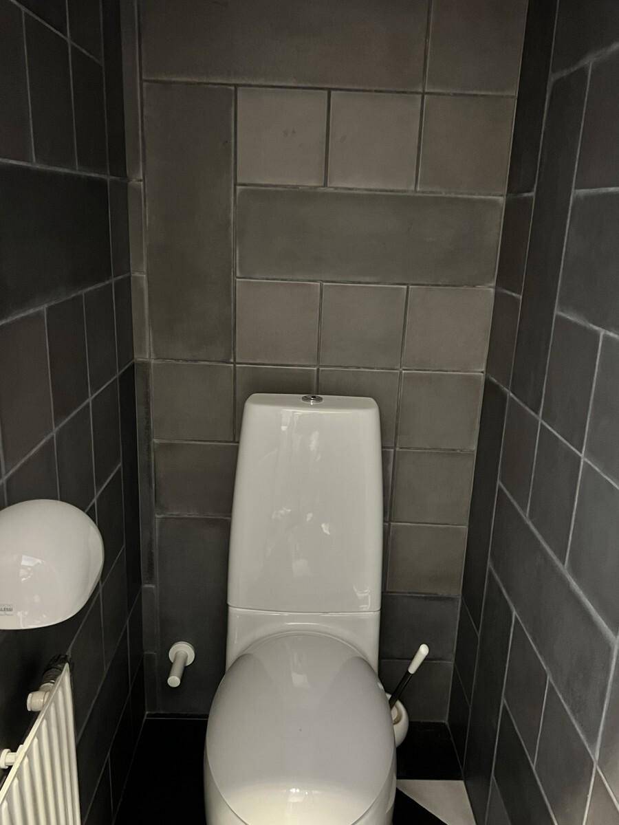 Separate Toilette mit grauen Wandfliesen und einem weißen Stand-WC, sauber und funktional.
