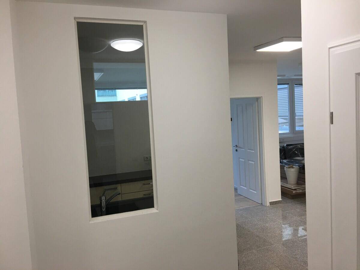 Heller Flur mit weiß gestrichenen Wänden und einem Fenster, das den Blick in die Küche freigibt.