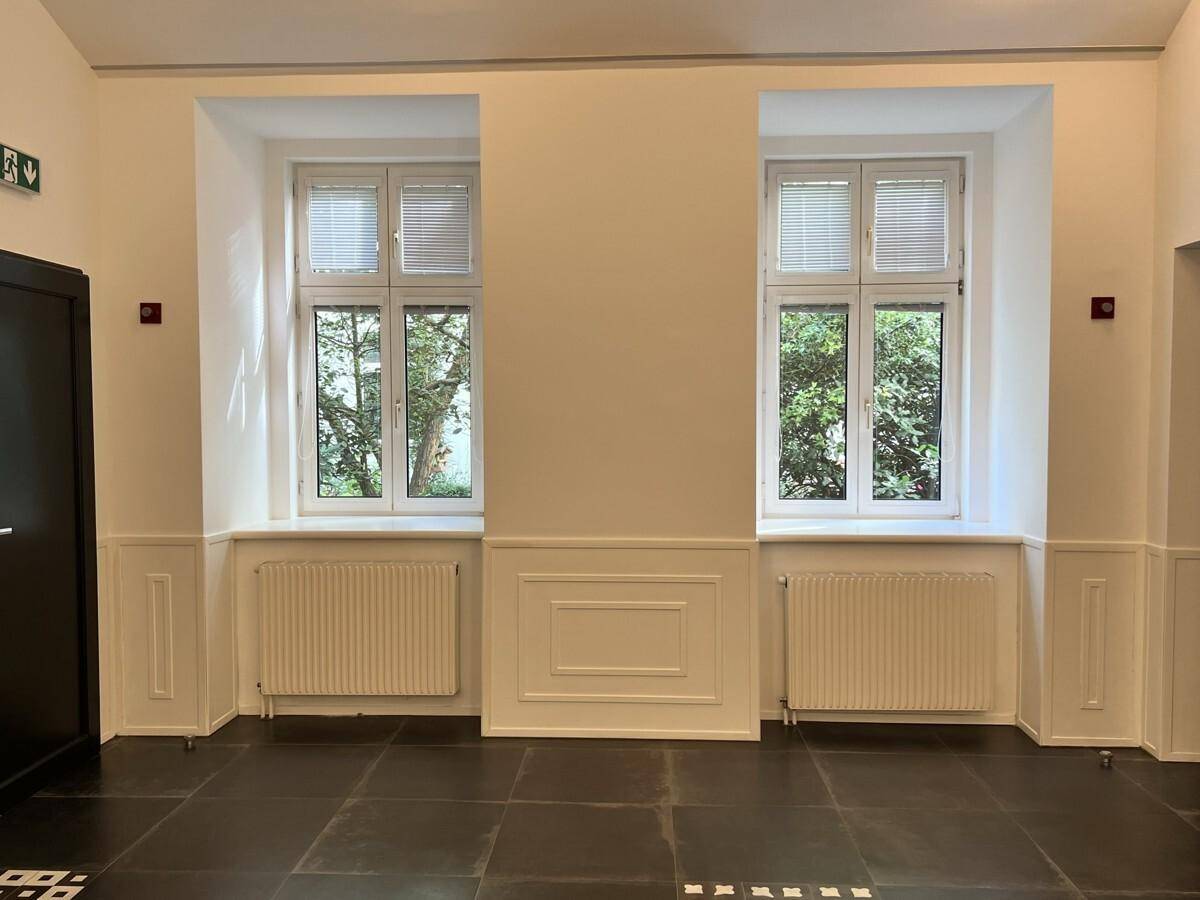 Heller Flur mit zwei großen Fenstern, die viel Tageslicht hereinlassen und einen Blick auf Bäume ermöglichen.