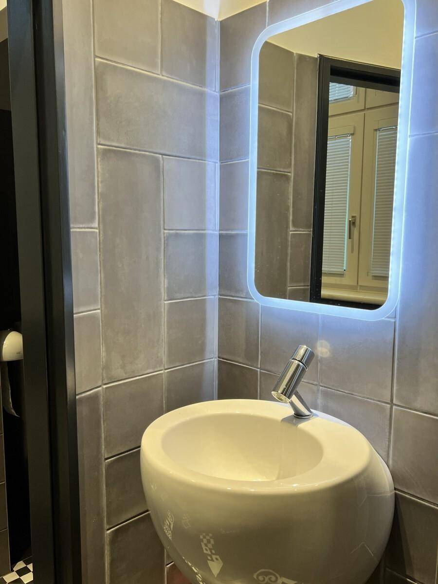 Modernes Badezimmer mit einem runden Waschbecken, beleuchtetem Spiegel und grauen Wandfliesen.