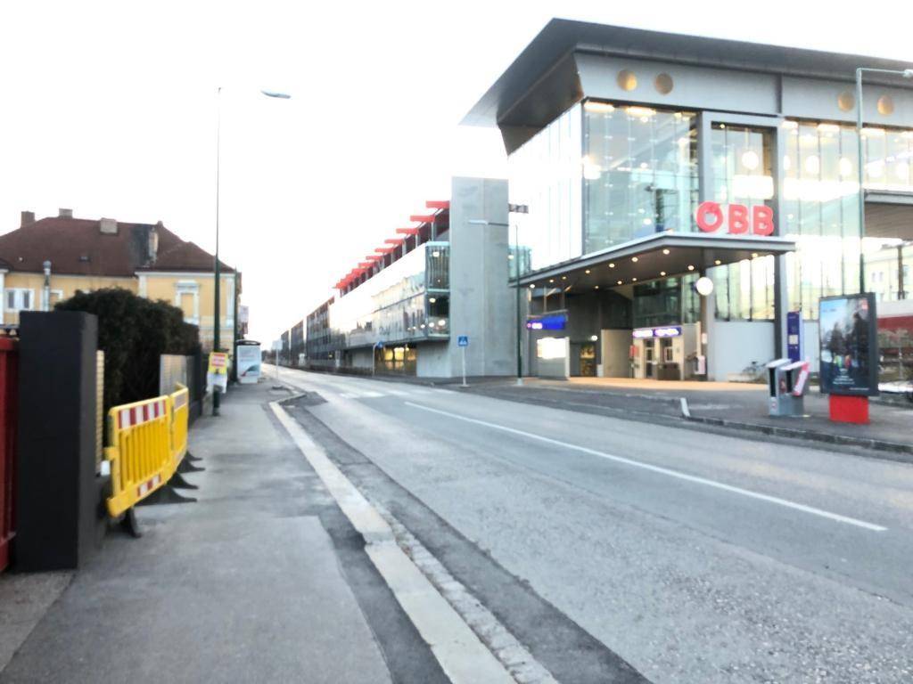 Weitläufiger Blick auf ein modernes Bahnhofsgebäude mit Glasfassade und die umliegende Straße in der Stadt.