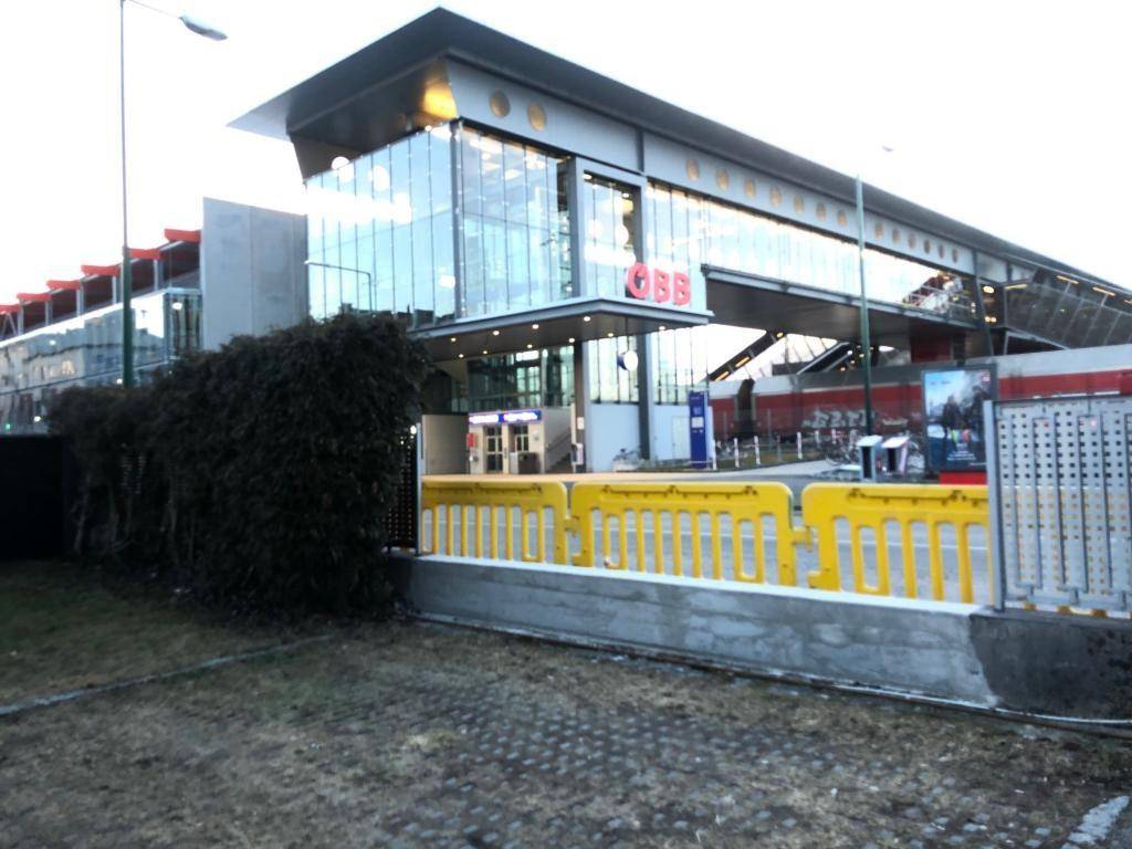 Modernes Bahnhofsgebäude mit großer Glasfassade und gelben Absperrungen im Vordergrund, bei Tageslicht aufgenommen.