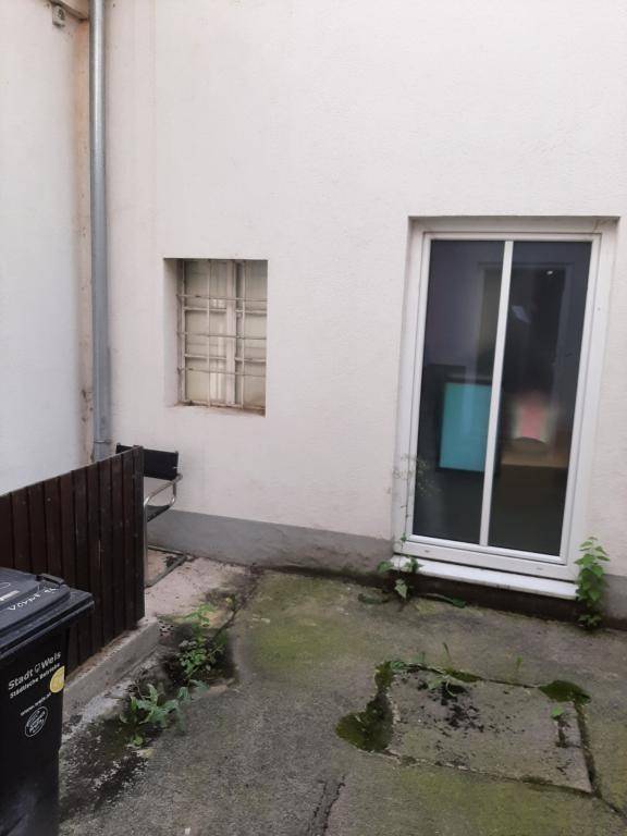 Kleiner, gepflasterter Hinterhof mit einer Tür, einem Fenster und einem Mülleimer.