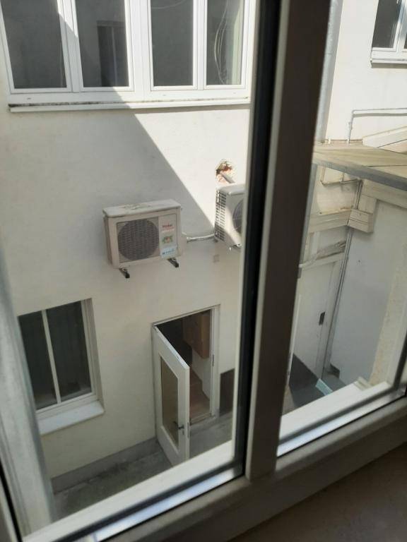 Blick aus dem Fenster auf einen kleinen Innenhof mit Klimaanlagen und einer Tür.