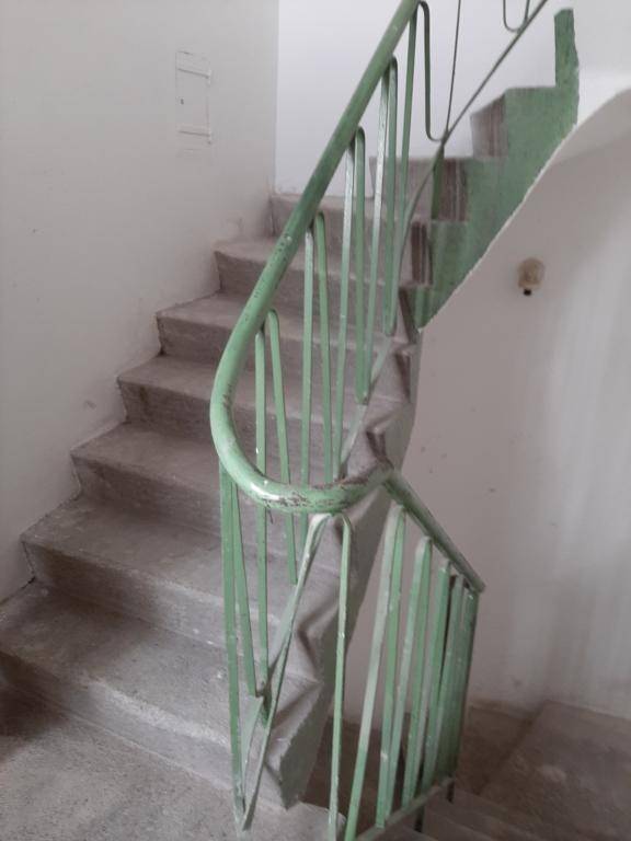 Altes Treppenhaus mit abgenutzten Stufen und einem grün gestrichenen Metallgeländer.