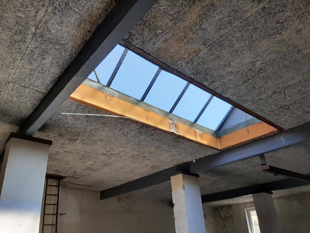 Detailaufnahme eines großen Oberlichts in einer Rohbaudecke mit sichtbaren Trägern.