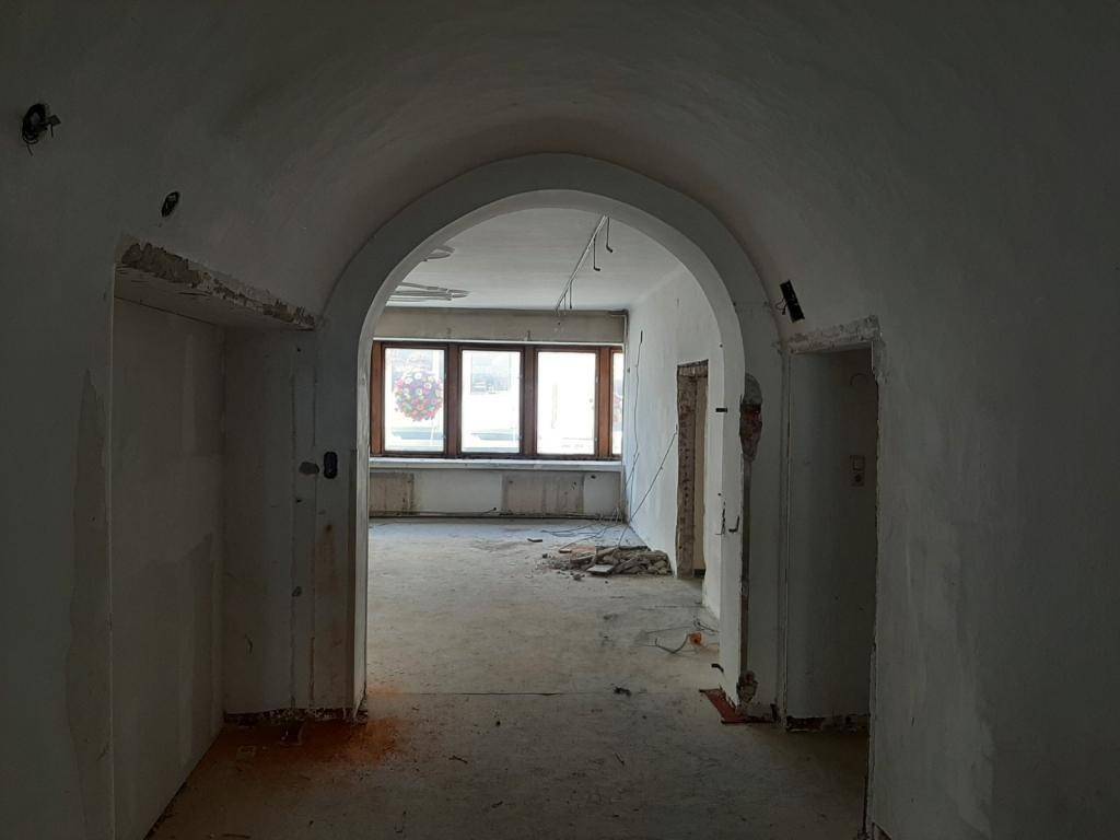 Gewölbter Durchgang führt zu einem weiteren Raum mit großen Fenstern, alles im Sanierungszustand.