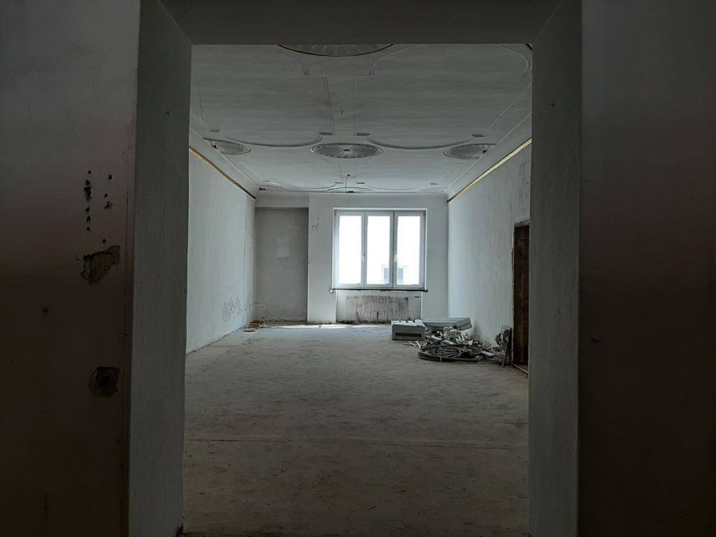 Blick durch einen Türrahmen in einen Raum mit Stuckdecken und einem großen Fenster, im Sanierungszustand.