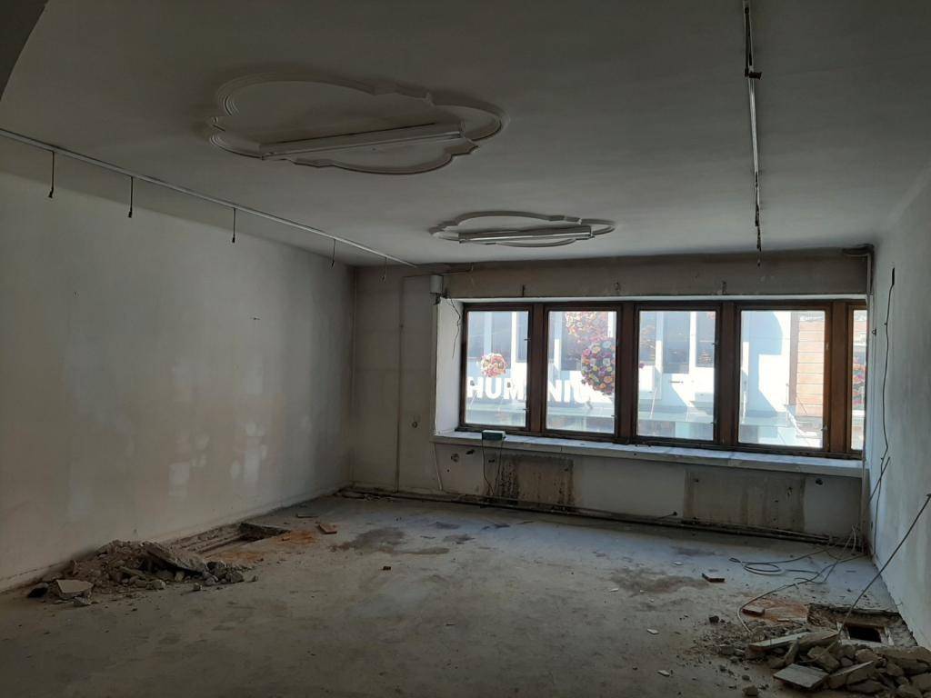 Raum im Sanierungszustand mit Stuckdecken und großen Fenstern, die auf die Straße blicken.