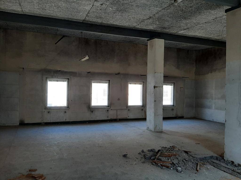 Großer, leerer Raum im Rohbau mit mehreren Fenstern und einer tragenden Säule.