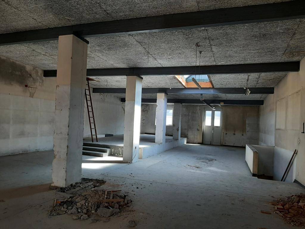 Geräumiger Innenraum im Rohbau mit Säulen, Deckenbalken und einer Leiter, bereit zur Neugestaltung.