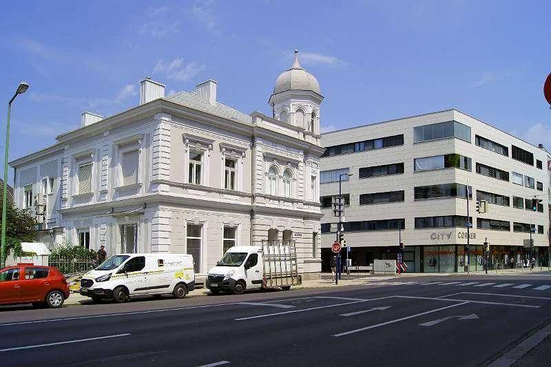 Straßenansicht mit einem historischen Gebäude und einem modernen Bürokomplex, die die städtische Architekturvielfalt zeigen.