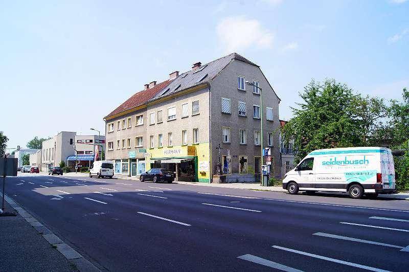 Straßenansicht mit einem mehrstöckigen Gebäude, das Geschäfte im Erdgeschoss und Wohnungen darüber beherbergt.