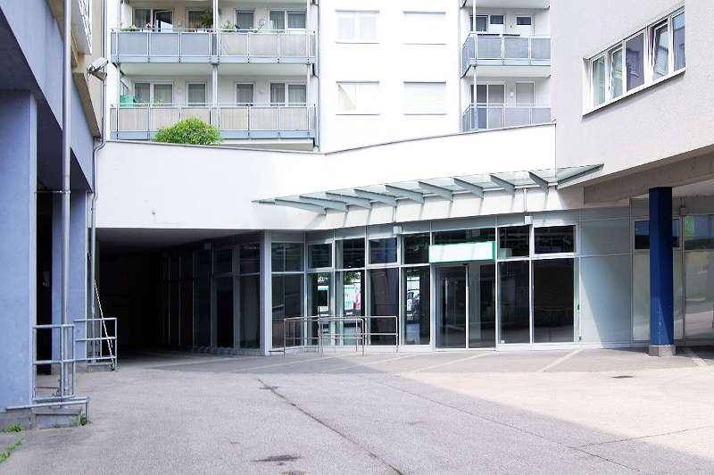 Eingangsbereich eines Geschäftsgebäudes mit Glasfassade und darüber liegenden Wohnbalkonen.