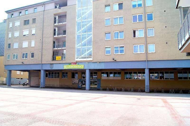 Großes Gebäude mit moderner Glasfassade und einem externen Glasaufzug, umgeben von einem Vorplatz.